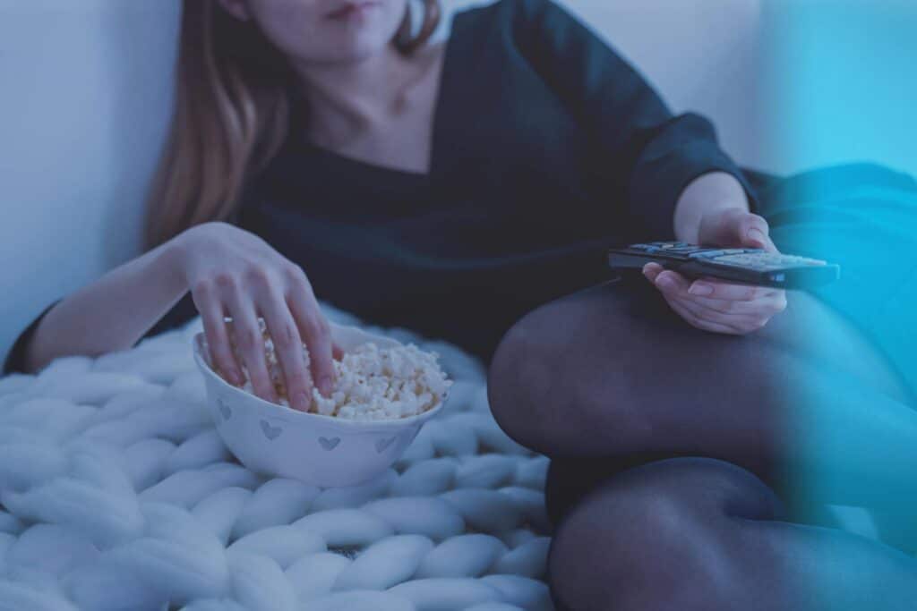 mujer mirando televisión desde la cama y comiendo palomitas